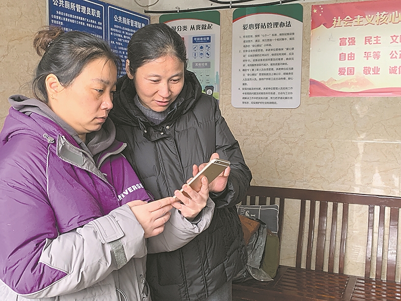 王莉(右)跟同事一起在手机上搜寻公厕信息。 记者 周娜 通讯员 鞠志清 李加胜 摄